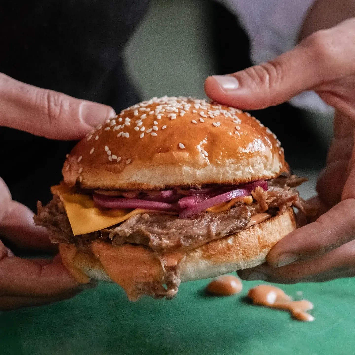 Cheddarlı, közlenmiş soğanlı bir Miante burgeri iki elle tutuluyor
