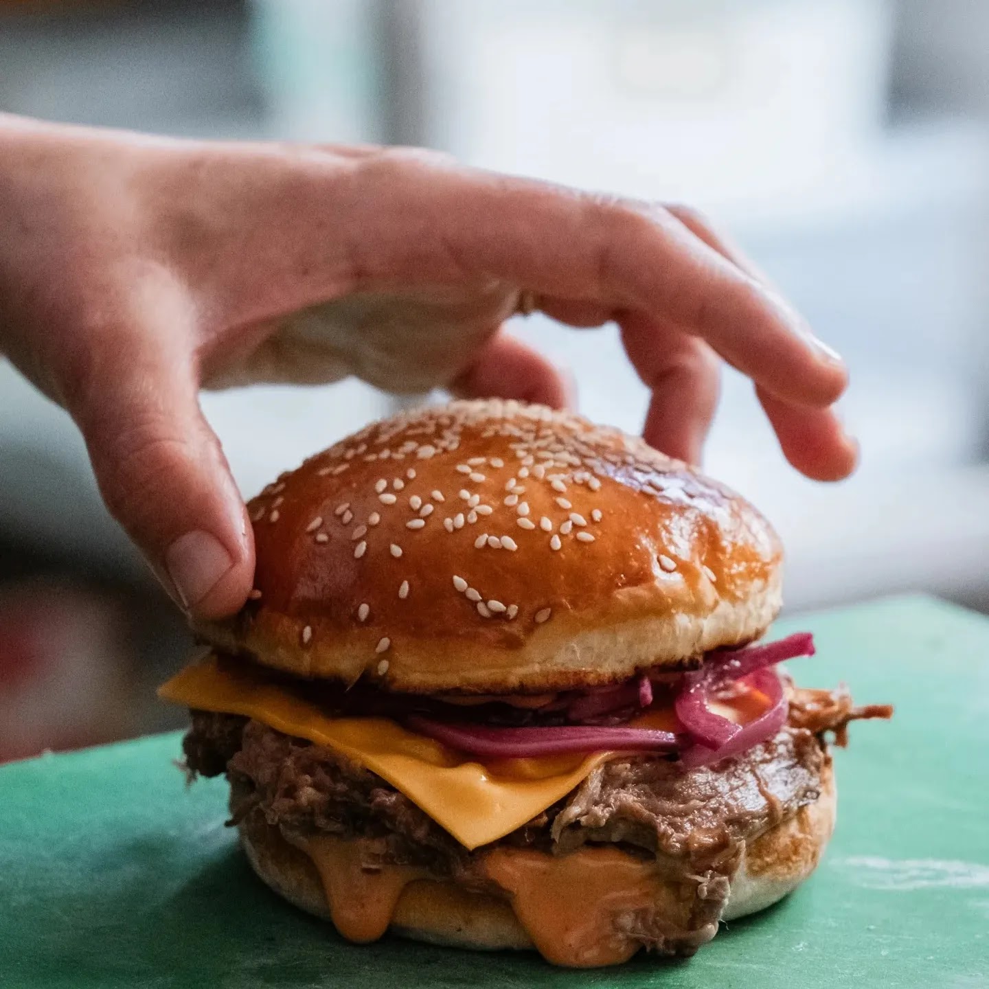 Susamlı ekmeği ve turşulu soğanıyla masada duran bir burger